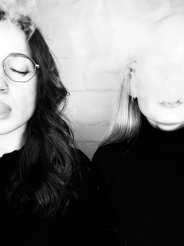 Artistic black and white photo of two women smoking indoors.